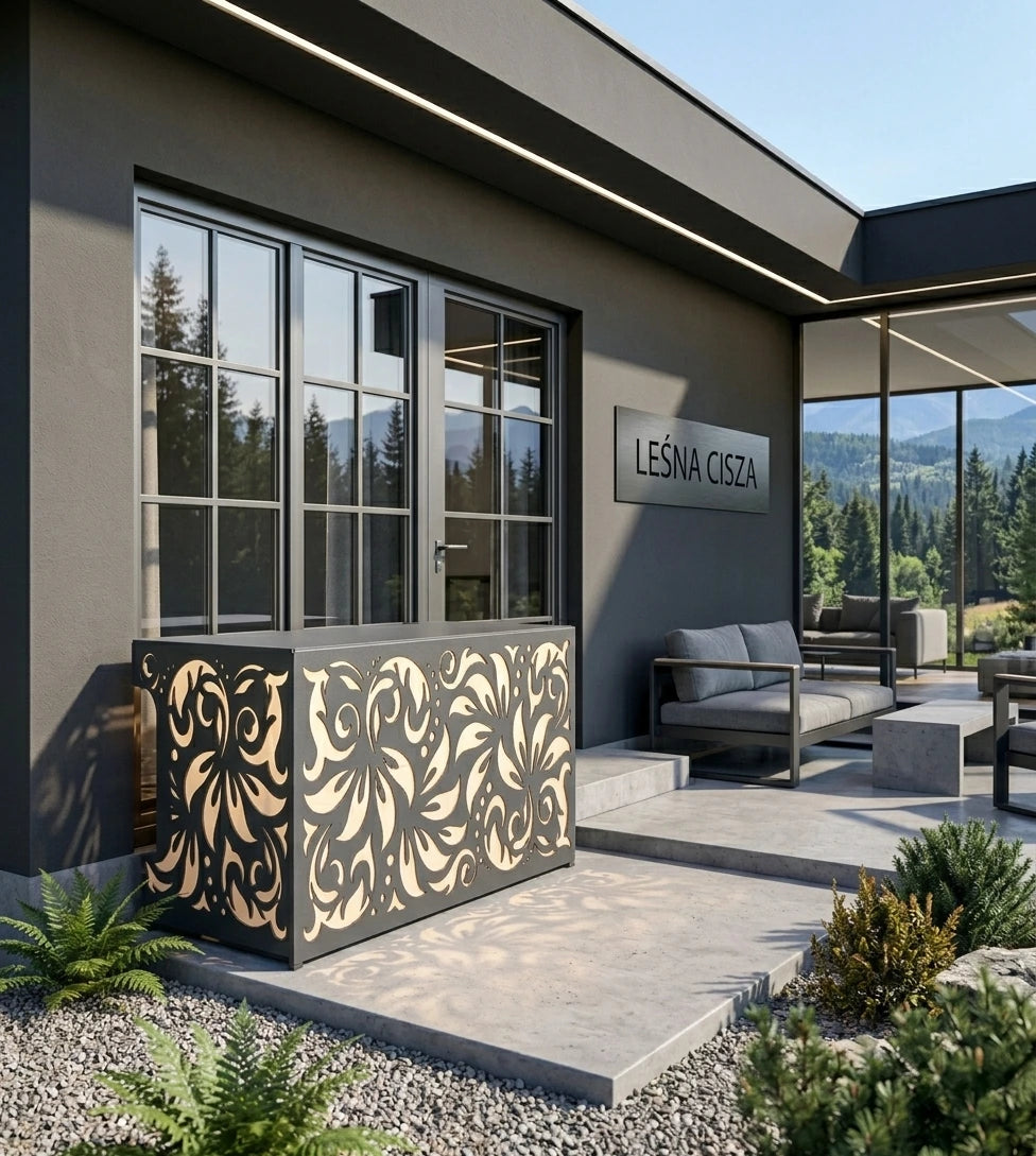 Modern outdoor patio area with a decorative black metal planter featuring an ornate gold-toned floral cutout pattern, set in front of a contemporary gray house with large windows 