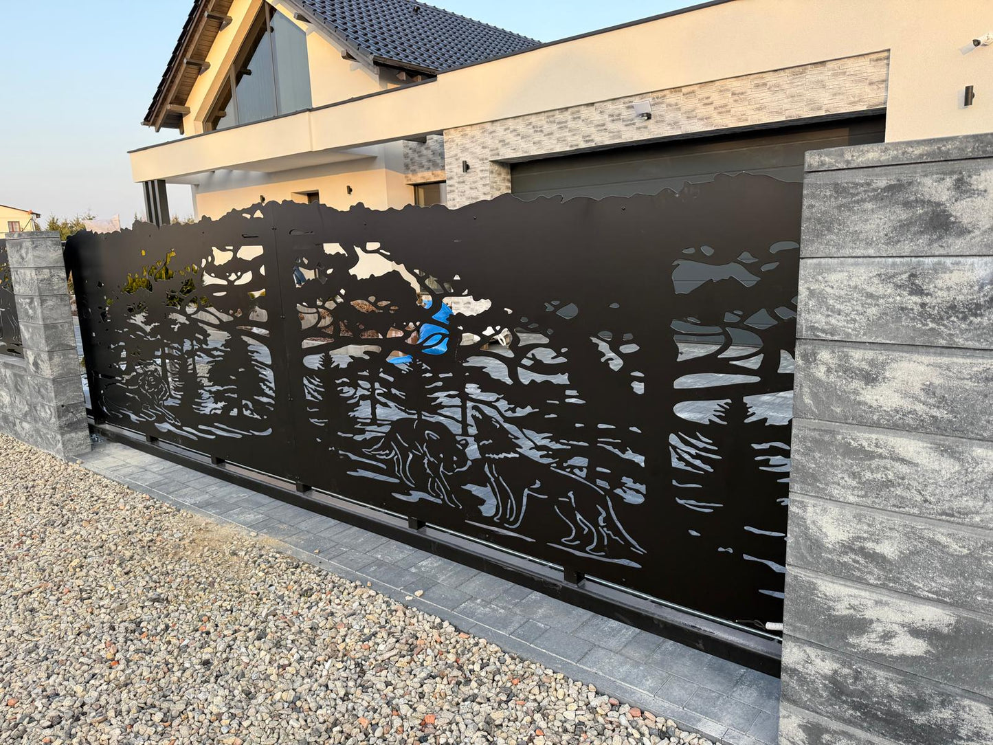 Modern black laser-cut sliding gate with a wolf and forest silhouette, installed at a contemporary house entrance.