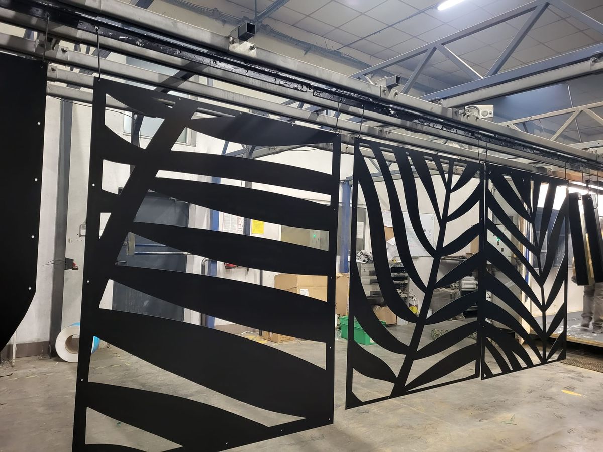 Black metal decorative panels with leaf patterns in a workshop setting