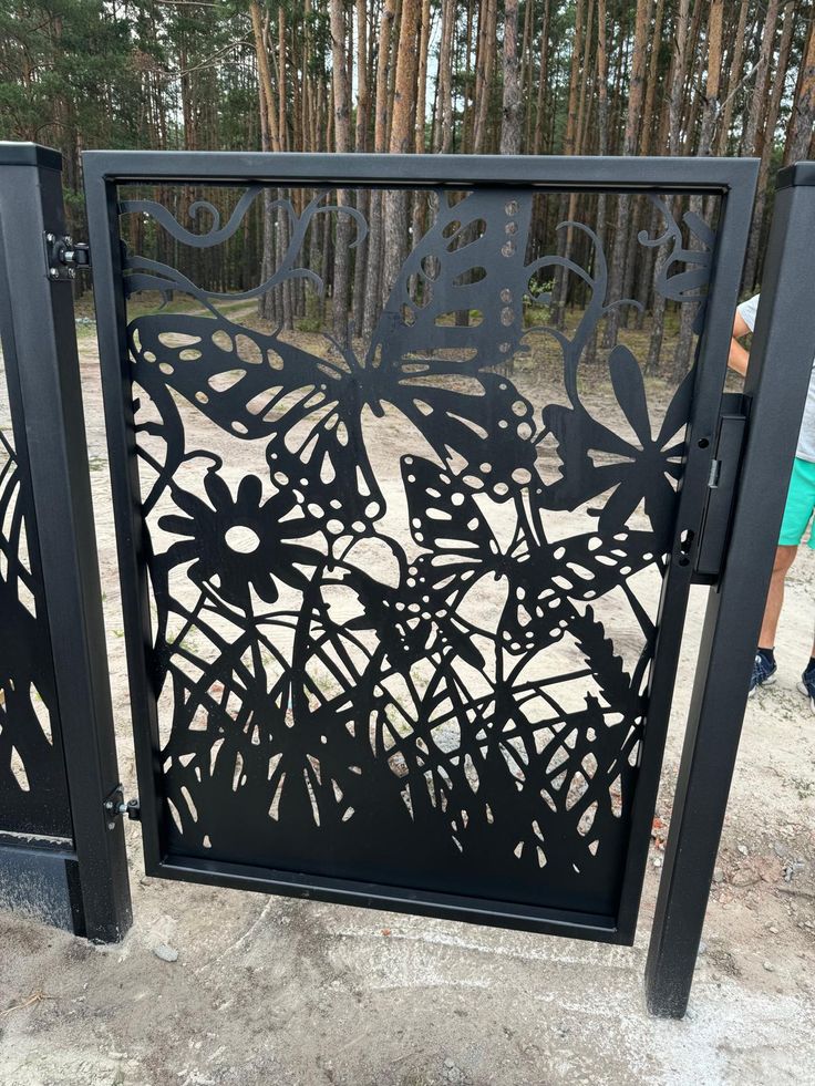 Decorative metal gate with butterfly and floral designs in a forest setting