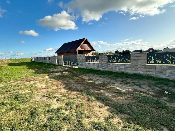 Wooden shed with a stone wall and grassy area under a blue sky with clouds.