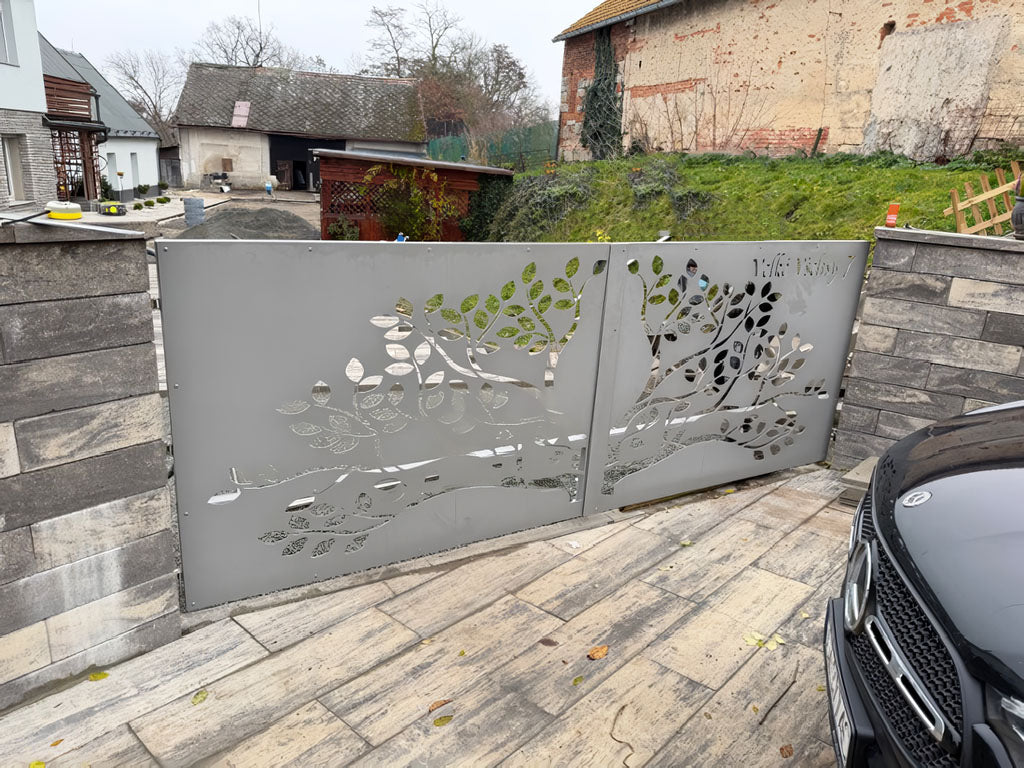 Decorative metal garden gate with leaf patterns on a stone patio, with a car partially visible.